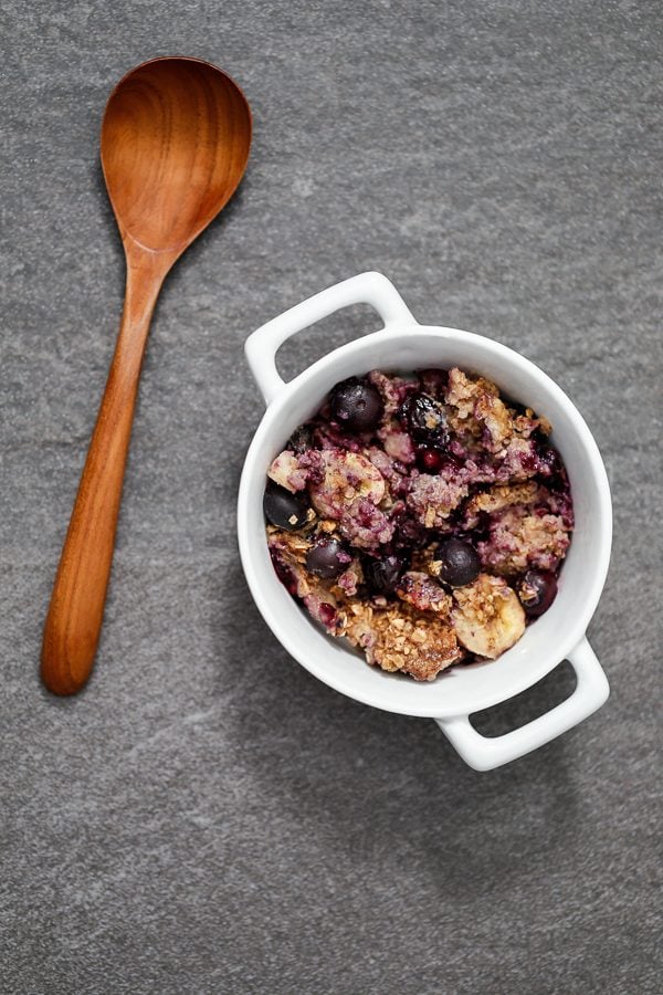 baked oatmeal including blueberries, walnuts, bananas, and oats in a container with a wooden spoon.