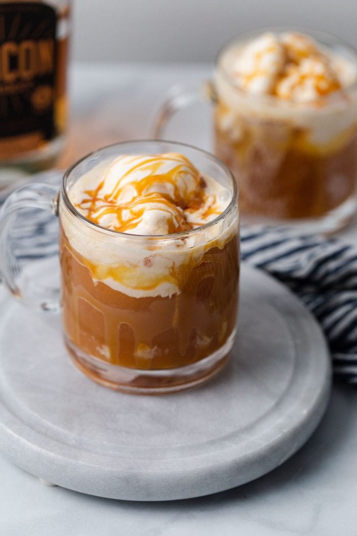 two clear glasses filled with apple cider and topped with ice cream and caramel sauce.