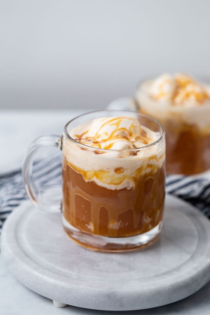 two clear glasses filled with apple cider and topped with ice cream and caramel sauce.