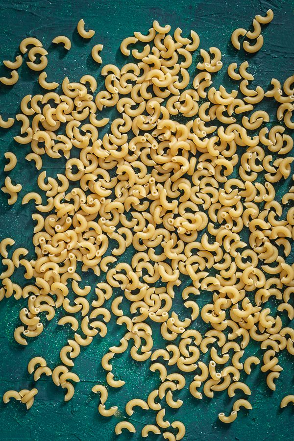 Yellow elbow noodles scattered on top of a green background. 