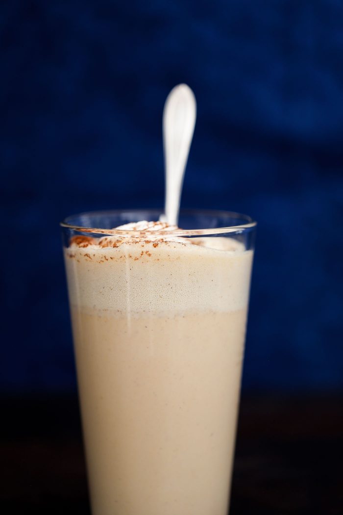a glass filled with a milkshake, whipped cream, cinnamon, and a spoon.