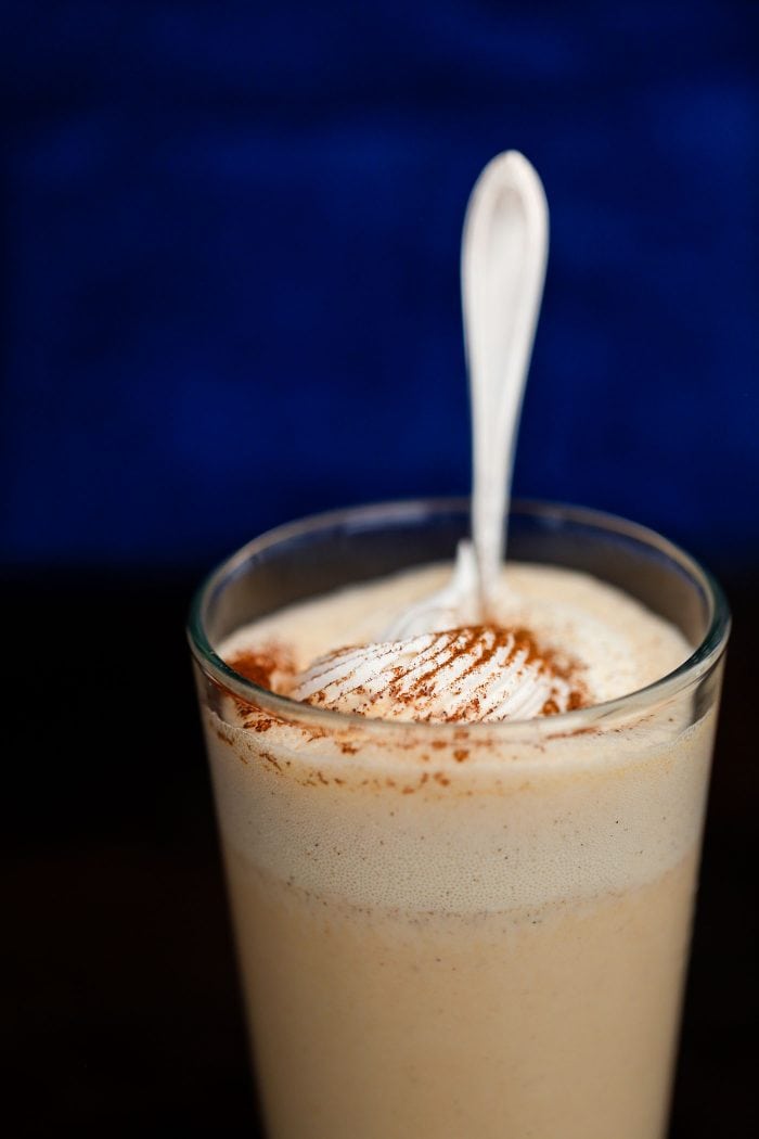 milkshake in glass with whipped cream and spices with a spoon.