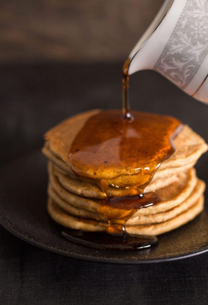 A stack of pancakes with syrup being drizzled onto the top.