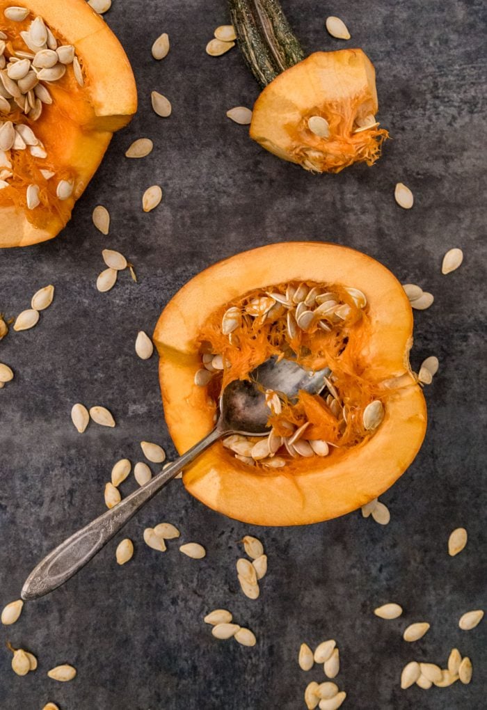 Two pumpkin halves face up exposing seeds with spoon and stem